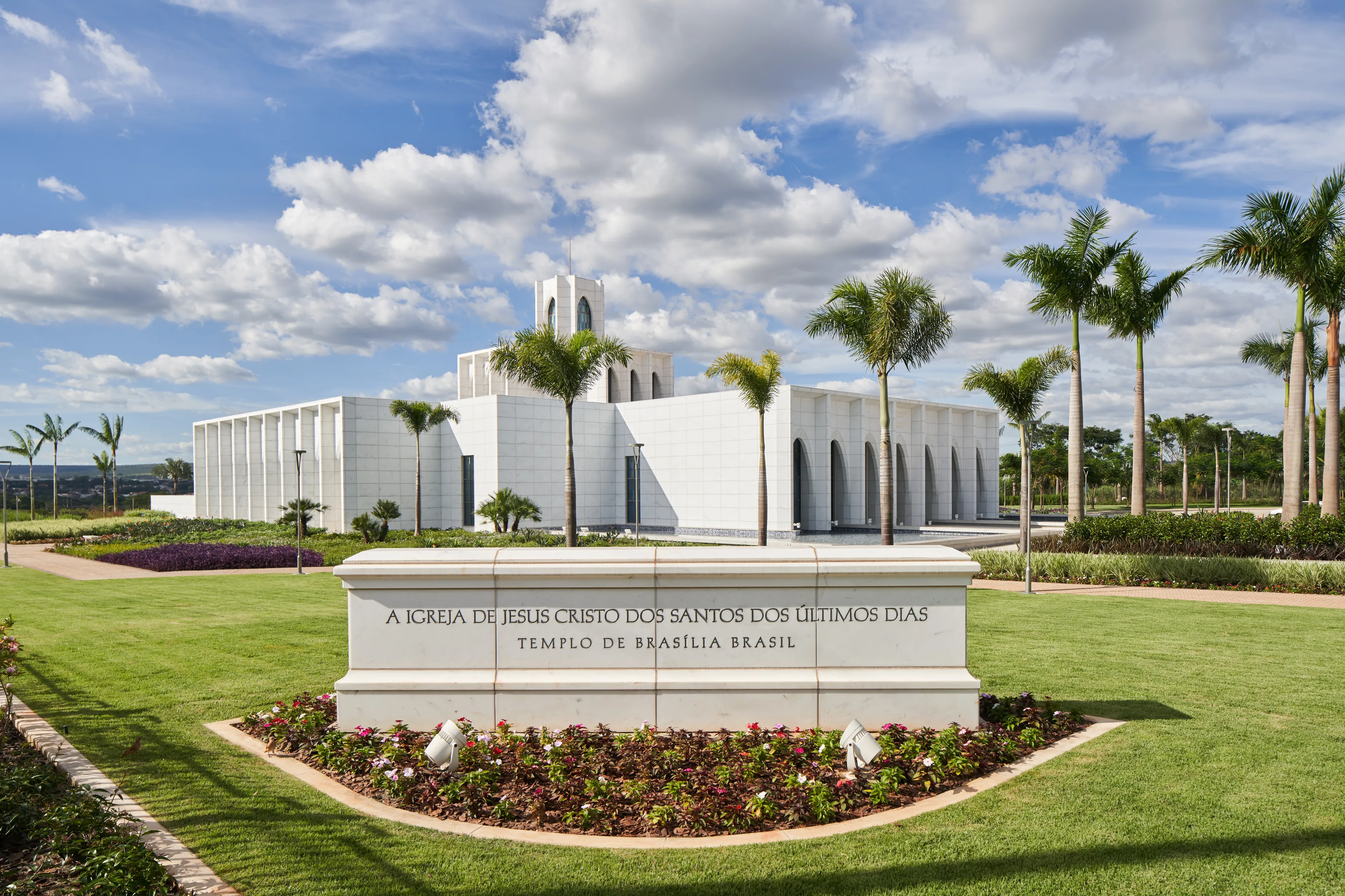 Exterior of the Brasilia Brazil Temple. It features the temple, the temple sign, and trees nearby. Image was taken during the day.