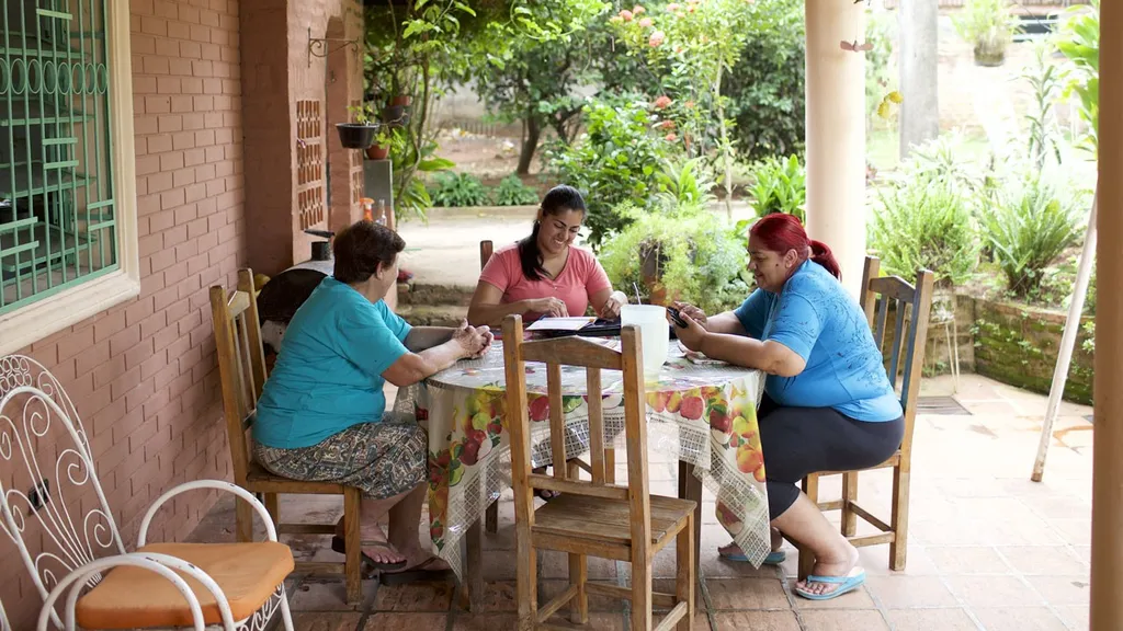 Paraguay.  Women sitting at an outdoor table with a laptop computer and family history pamphlets.