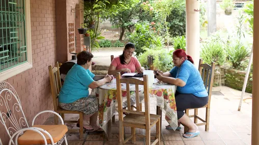 Paraguay.  Women sitting at an outdoor table with a laptop computer and family history pamphlets.
