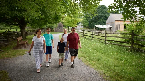 Various people walk the paths around the Sacred Grove. There are lots of trees around and everything is very green. The families are all walking on dirt pathways.