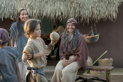 Nephi's wife sits outside with the children as they play.