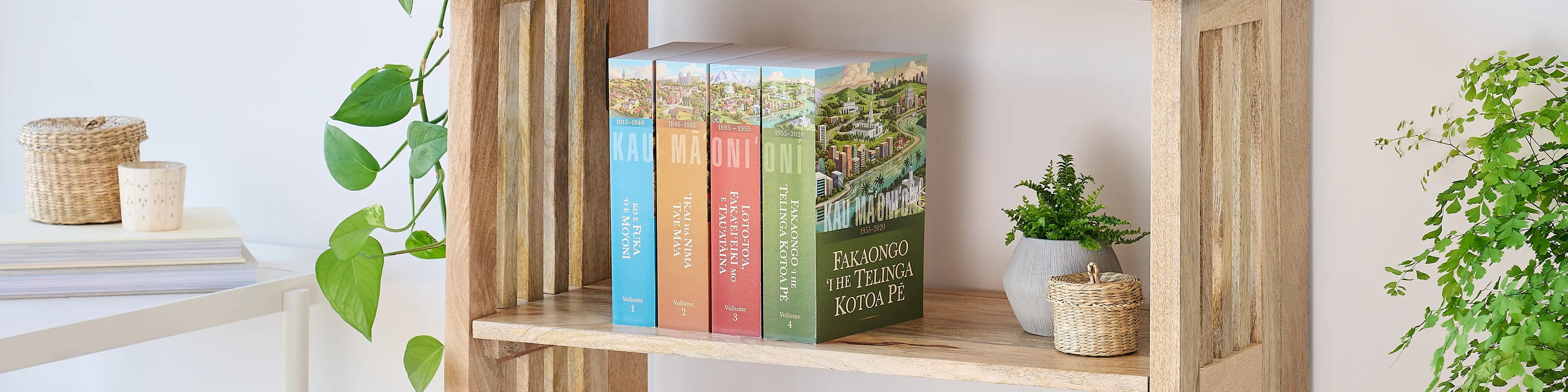 Picture of the book series, 'Saints' volume 1-4 (Tongan edition). Four volumes are arranged on the middle shelf of a wooden bookshelf along with plants.
