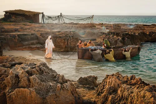 Christ standing in water and holding a rope attached to a boat that is being pushed by seven fishermen.
