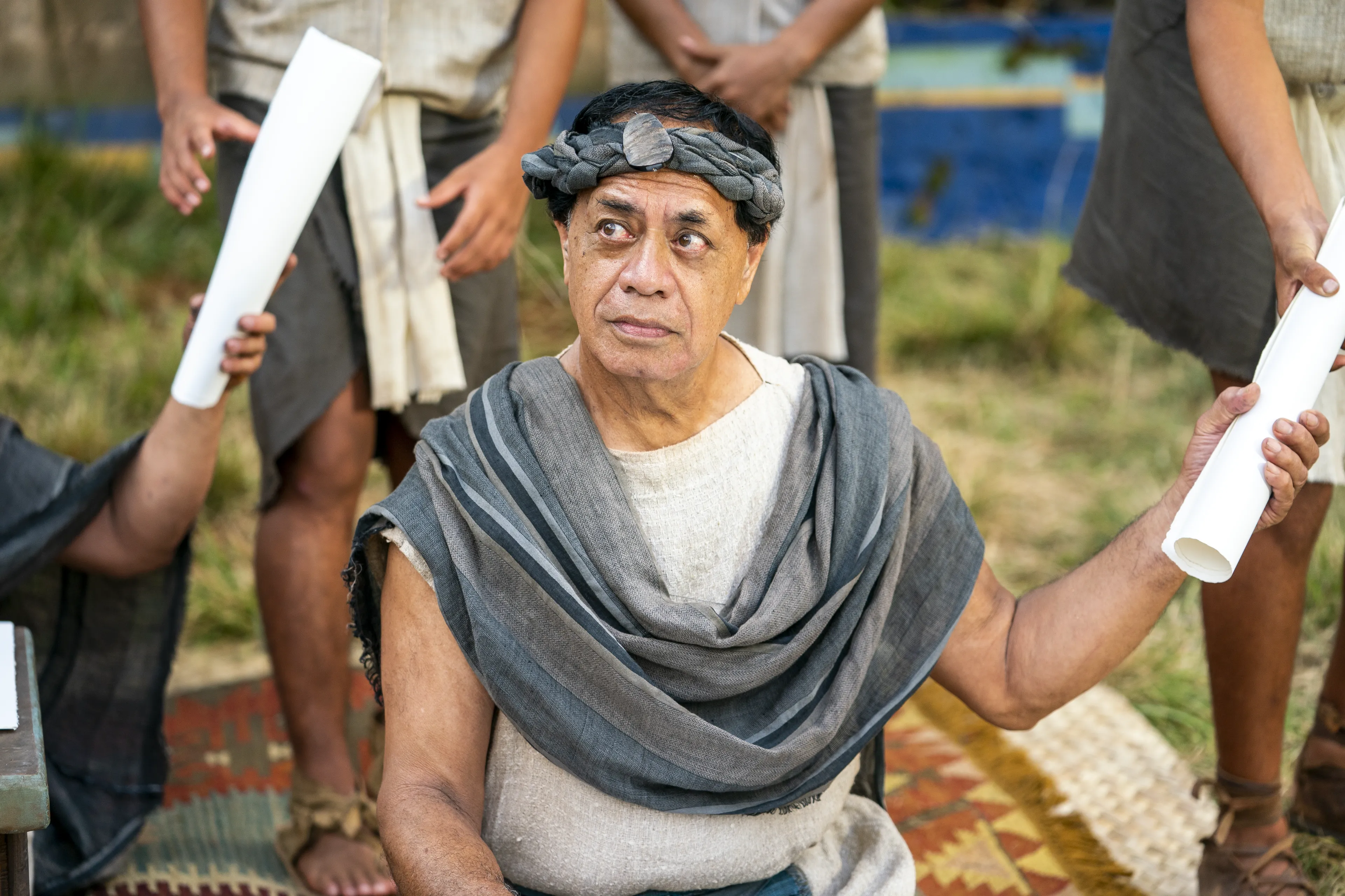 Some scribes sit, taking notes of what King Benjamin is teaching to the people in the Land of Zarahemla. They hand rolled parchment papers to runners who take the messages to the Nephites.