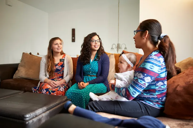 Two sister missionaries teach a woman in her living room about the Book of Mormon and the gospel of Jesus Christ