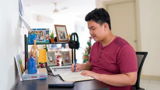   A young man sits in his home in Malaysia. He is studying.  