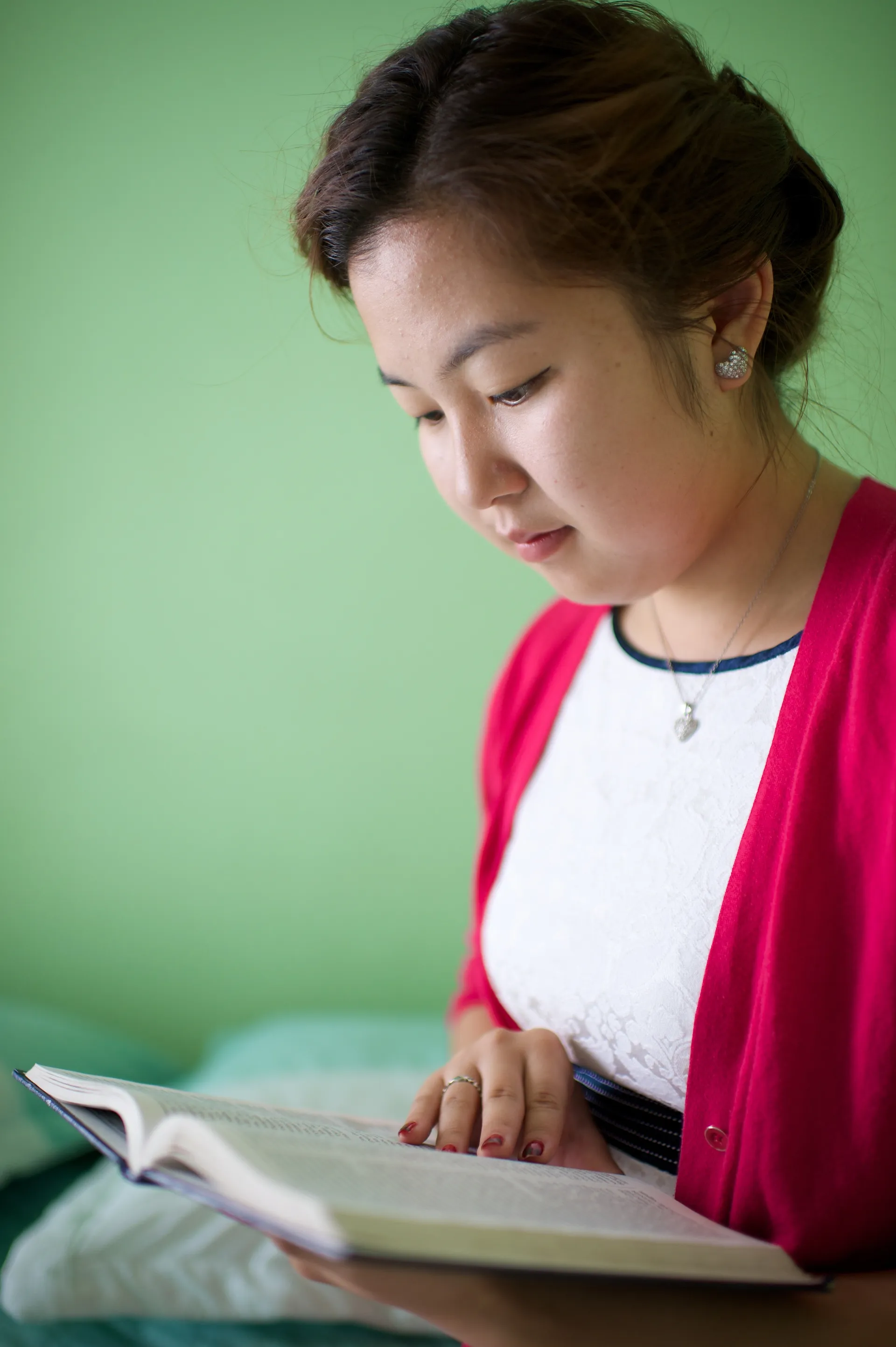 A young woman sits on her bed and reads from her scriptures.