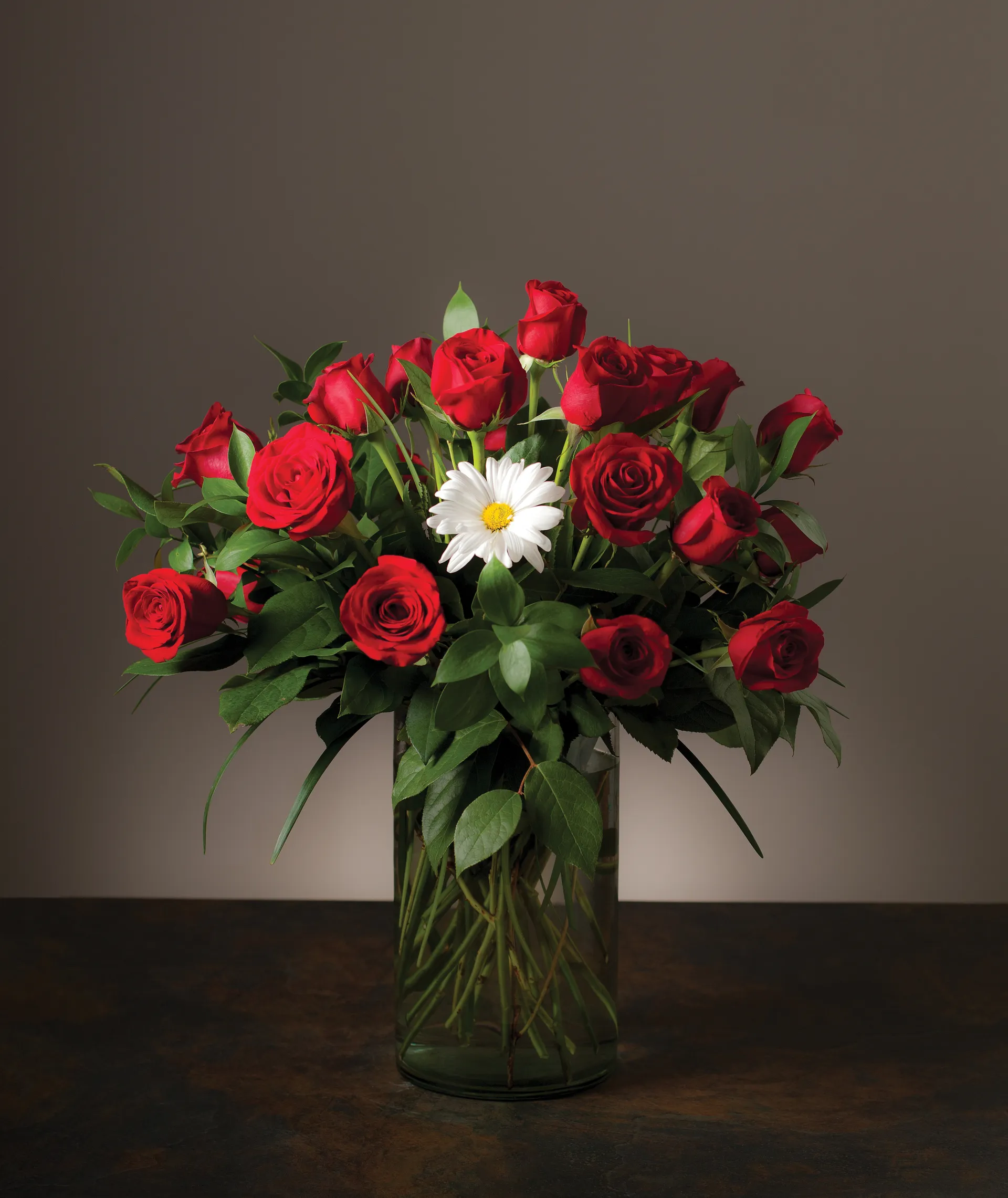 A white daisy in a vase full of red roses.