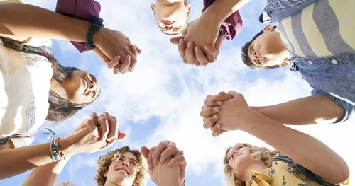 A group of young men and young women hold each other’s hands in a circle