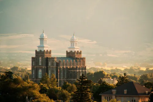 A view of the Logan Utah Temple and surrounding area in the late afternoon, with trees and the tops of houses all around.