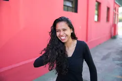 A young woman smiles in front of a pink house