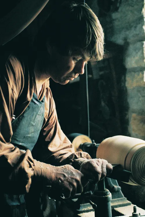 A man working indoors on a lathe.