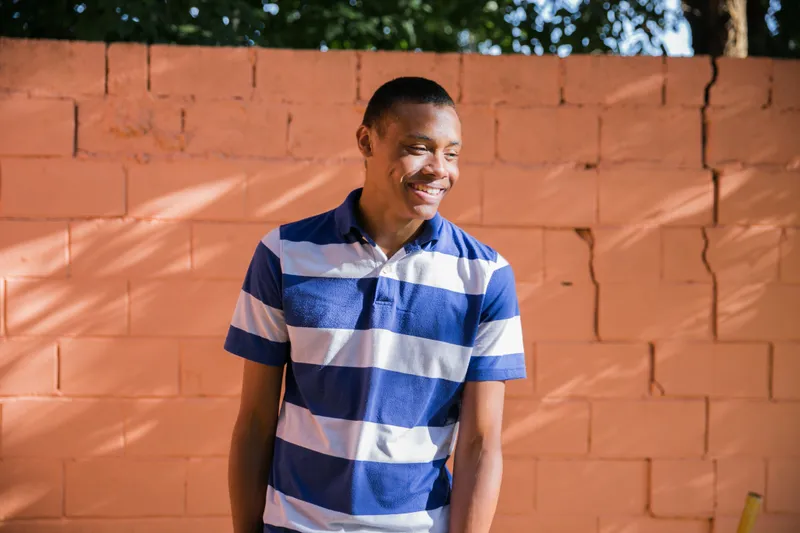 A young man stands against and orange brick wall