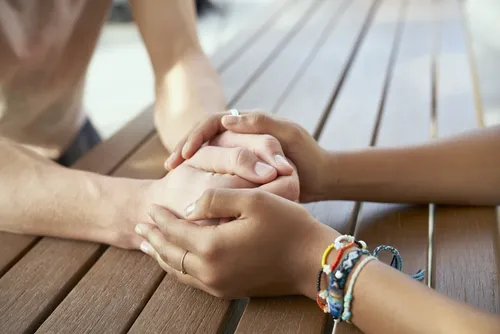 Two young women sit across from each other at a table. They are holding each others hands in what appears to be a way to comfort the other.