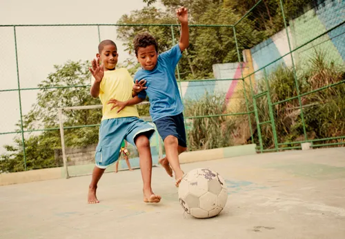two boys playing soccer on dirt field