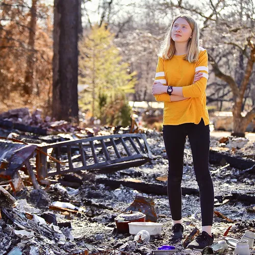 girl standing amid ashes of burned-down home