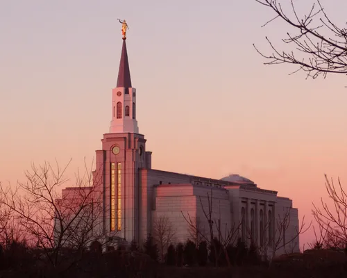 A front side view of the Boston Massachusetts Temple during sunset in the winter, with bare trees on the grounds.