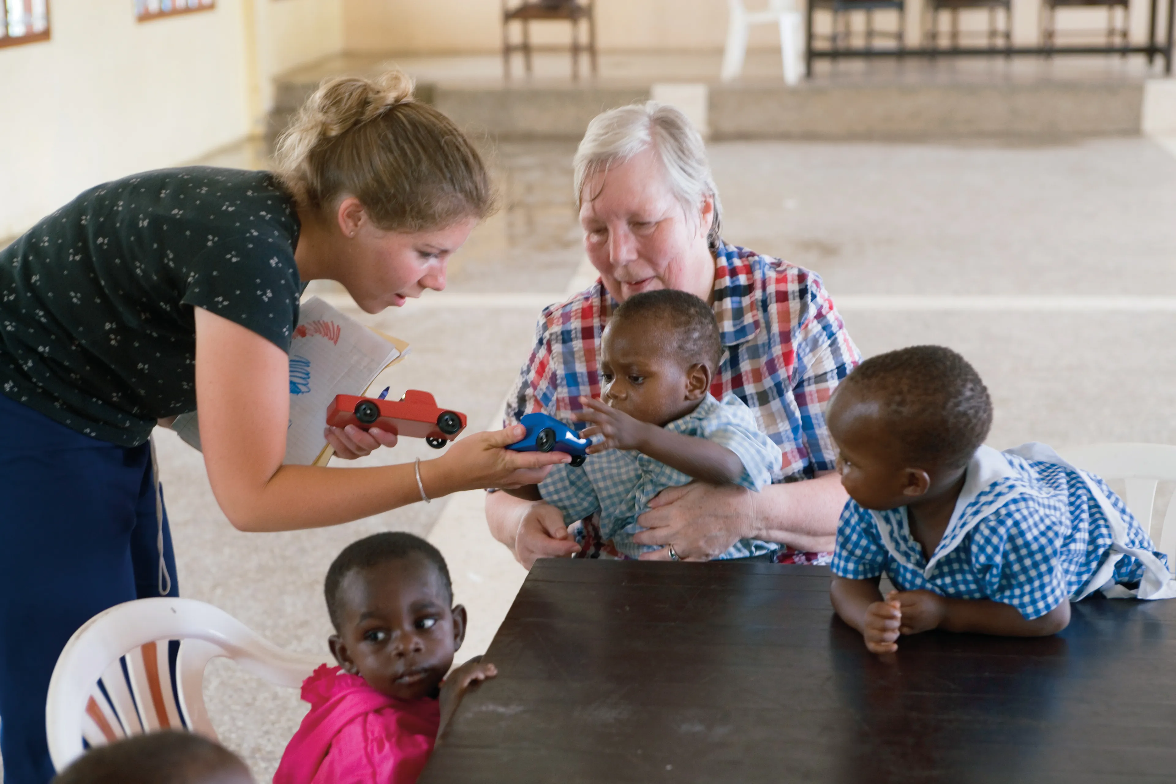 Two women with three African children at a table inside an orphanage.