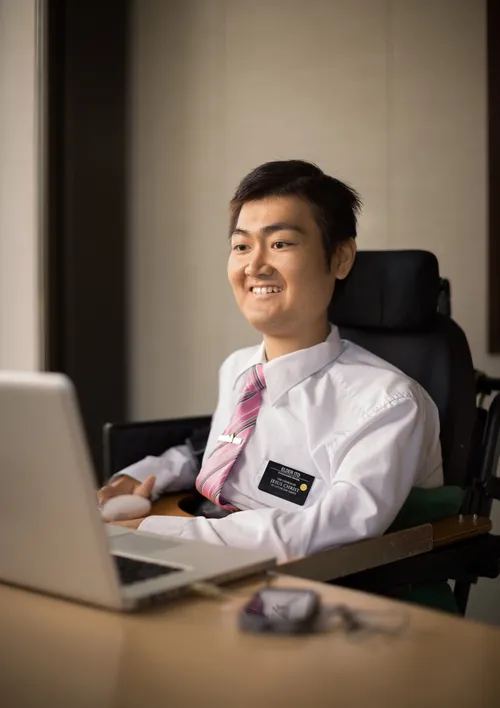 A Church-service missionary in a white shirt and tie sits at a desk and works on a laptop.