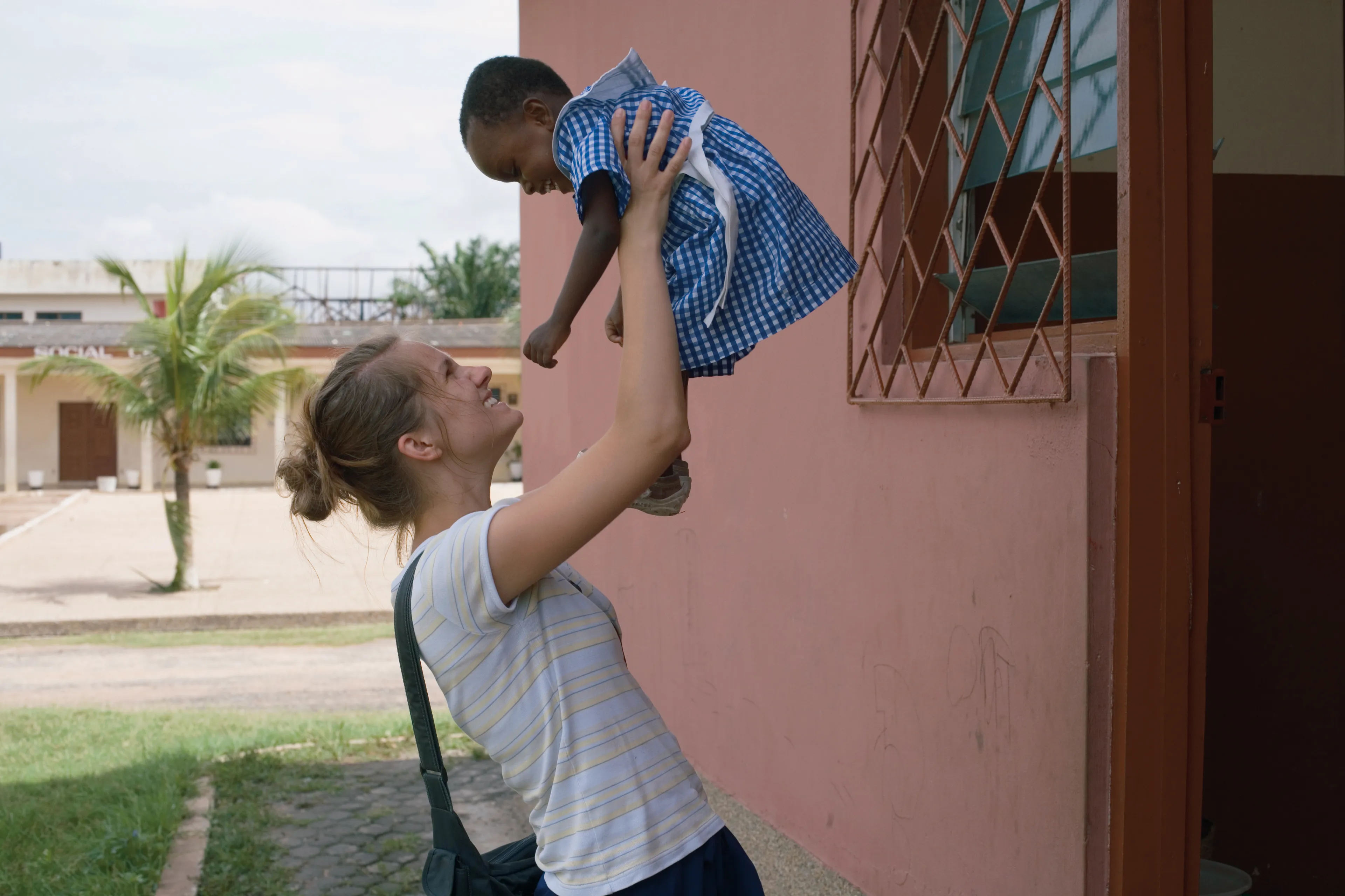 A woman smiling and holding up a little girl from Africa high in the air.