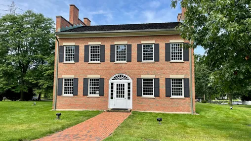 A large two-story, red-brick building with large, multi-paned windows and an arched doorway over the white door.
