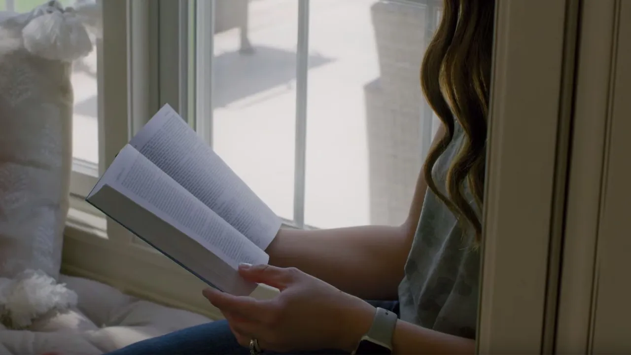 A woman sits in her window sill studying the Book of Mormon and the gospel of Jesus Christ