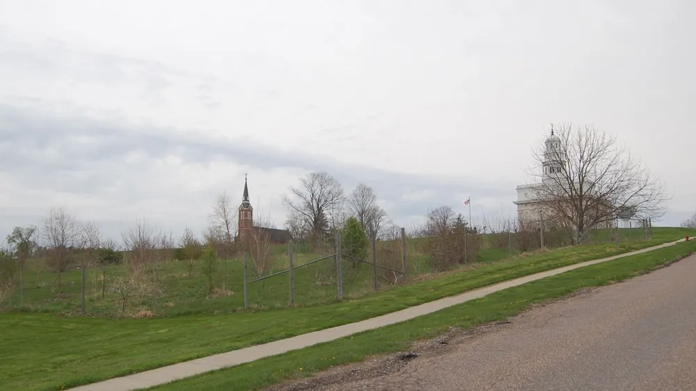 A fenced-in grouping of small trees with a brick church and white stone temple uphill in the background. 