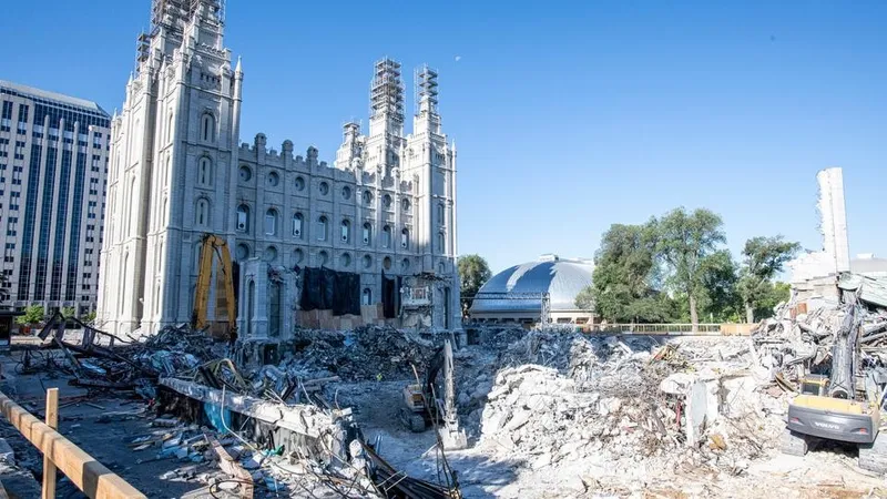 The Salt Lake Temple is under construction. The grounds are torn up and large trucks are in the midst of the debris. Part of the temple has a tarp over the side.  