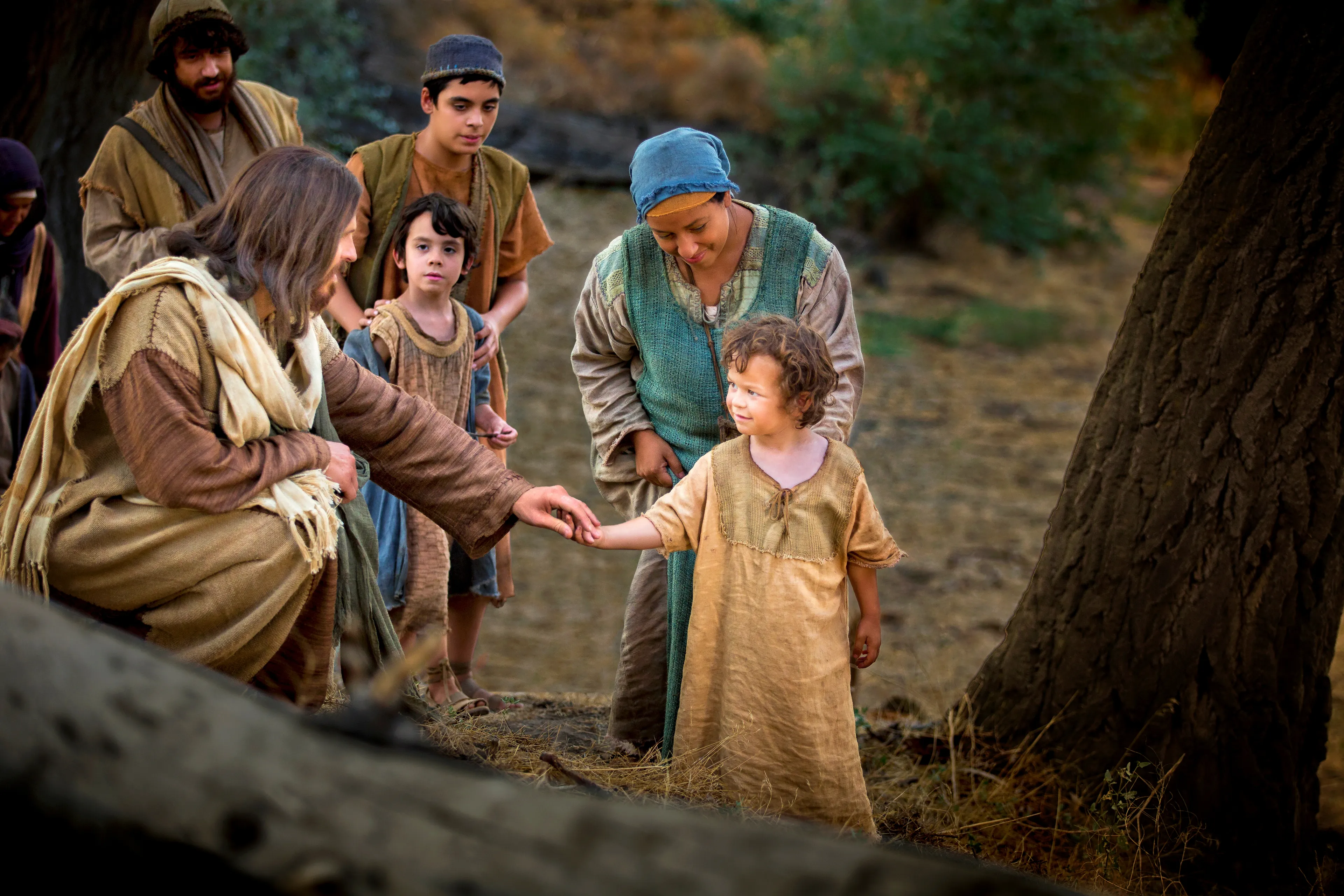 Christ sitting down and reaching for a child’s hand.