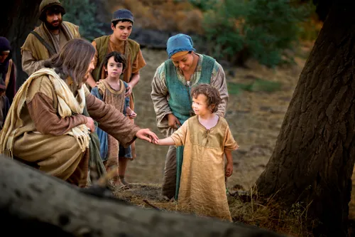 Christ sitting outside by a tree and holding a child’s hand, with others in the background.