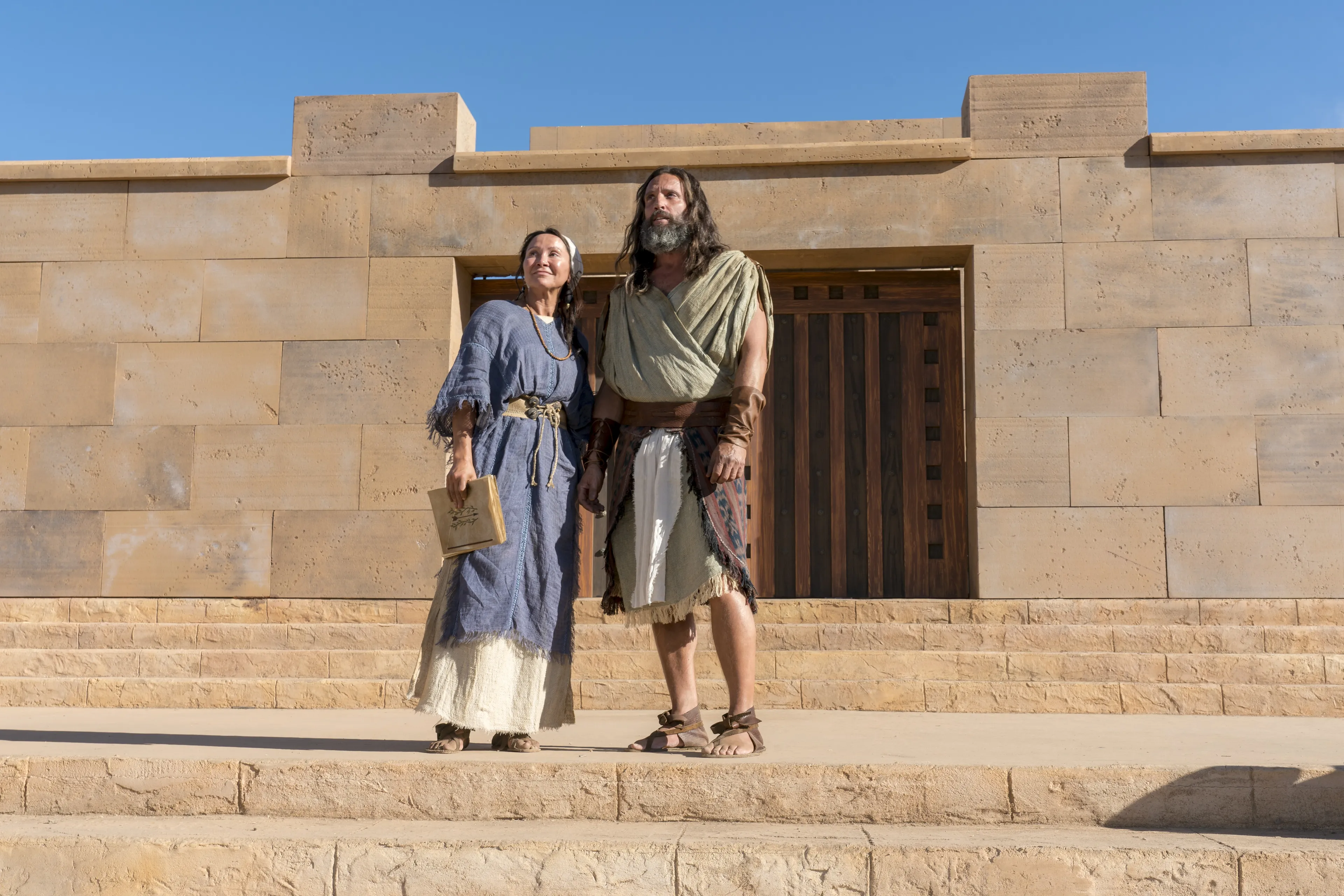 Nephi and his wife stand on the steps of the temple in the Land of Nephi.