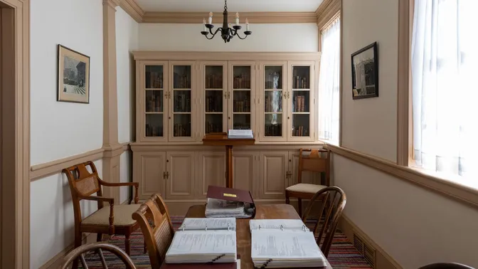 Interior room with chairs arranged around a wooden table and a built-in bookcase along the wall.