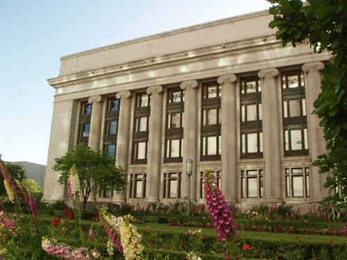 A view of the columns on the side of the Church Administration Building, with pink and white flowers seen in the foreground.