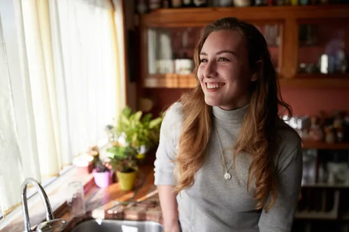 A young woman smiles as she stands in her home.