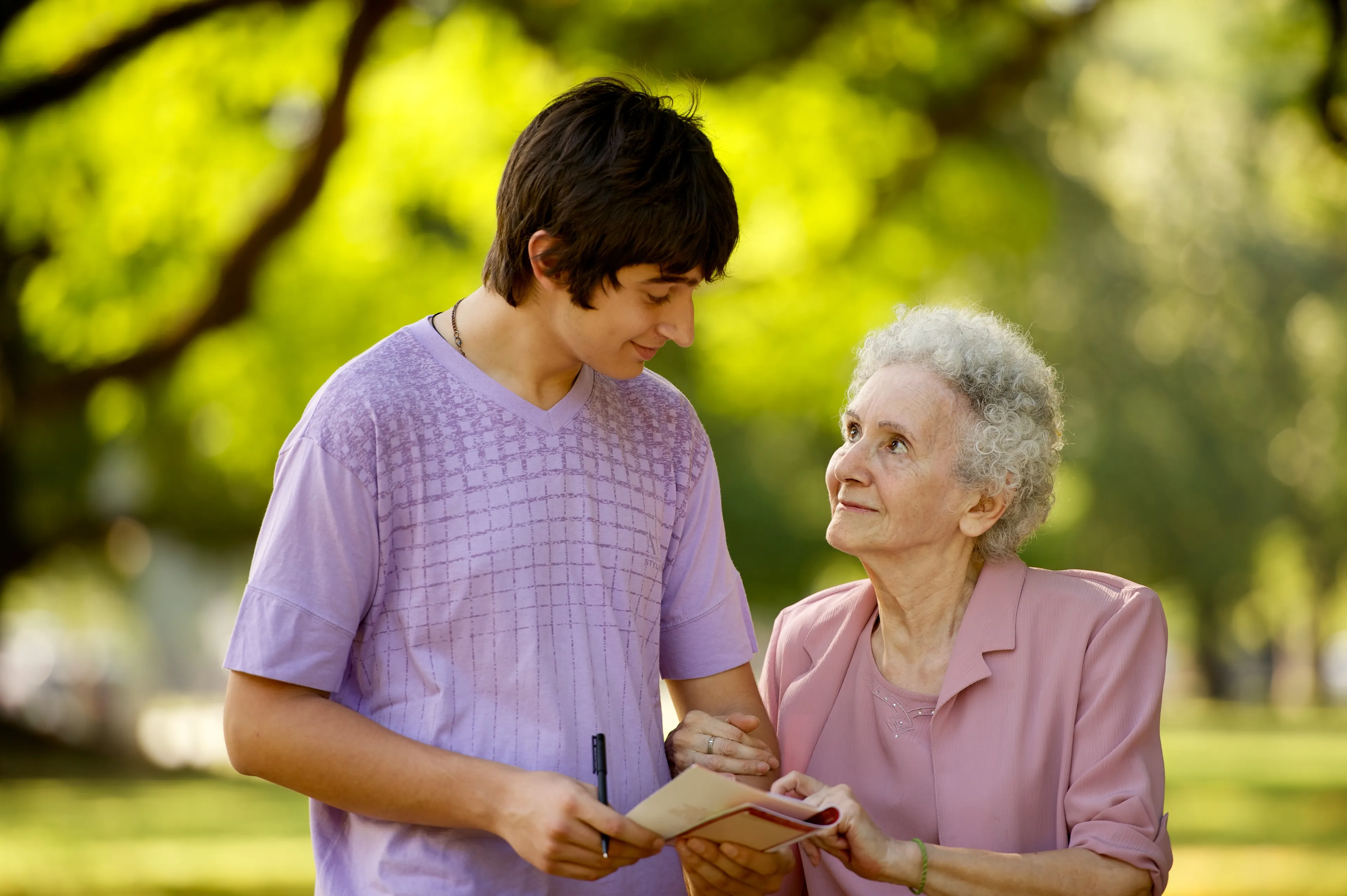 A young man smiles at an elderly woman as they walk with linked arms.