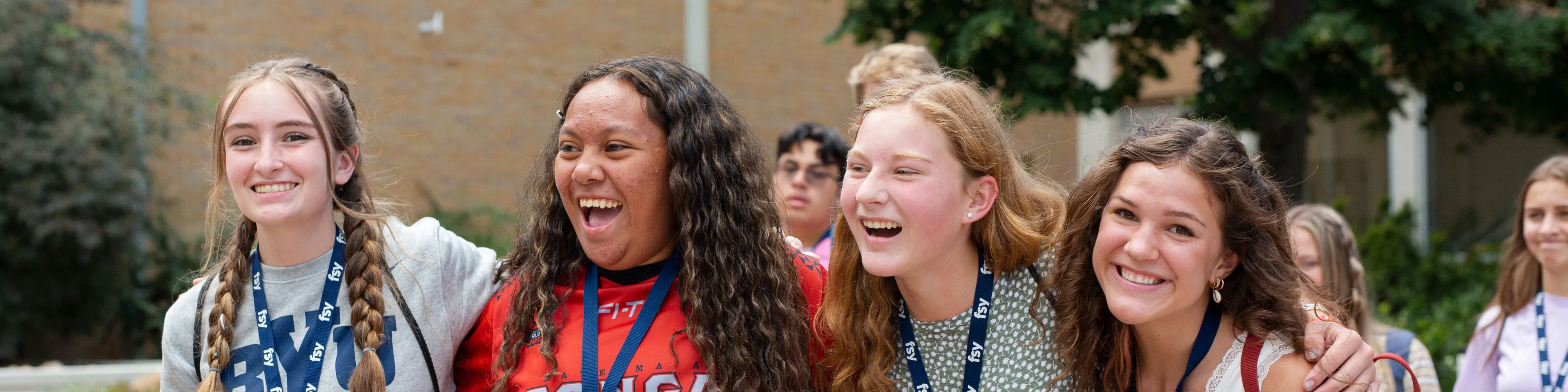 A group of smiling young women at FSY standing with their arms around each other's shoulders.