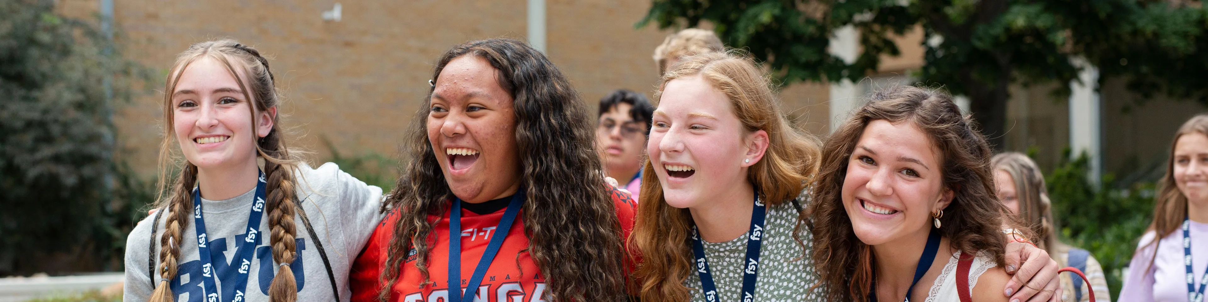 A group of smiling young women at FSY standing with their arms around each other's shoulders.