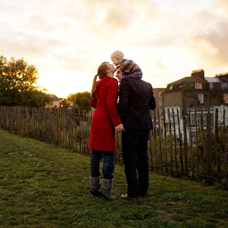 A mother and father stand in a field with their young son on the father’s shoulders