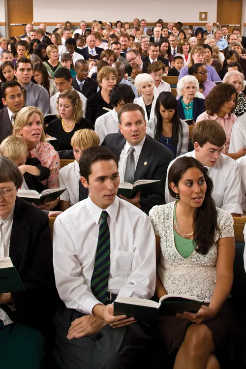 A large congregation in their Sunday best, sitting in the chapel, holding hymnbooks, and singing together.