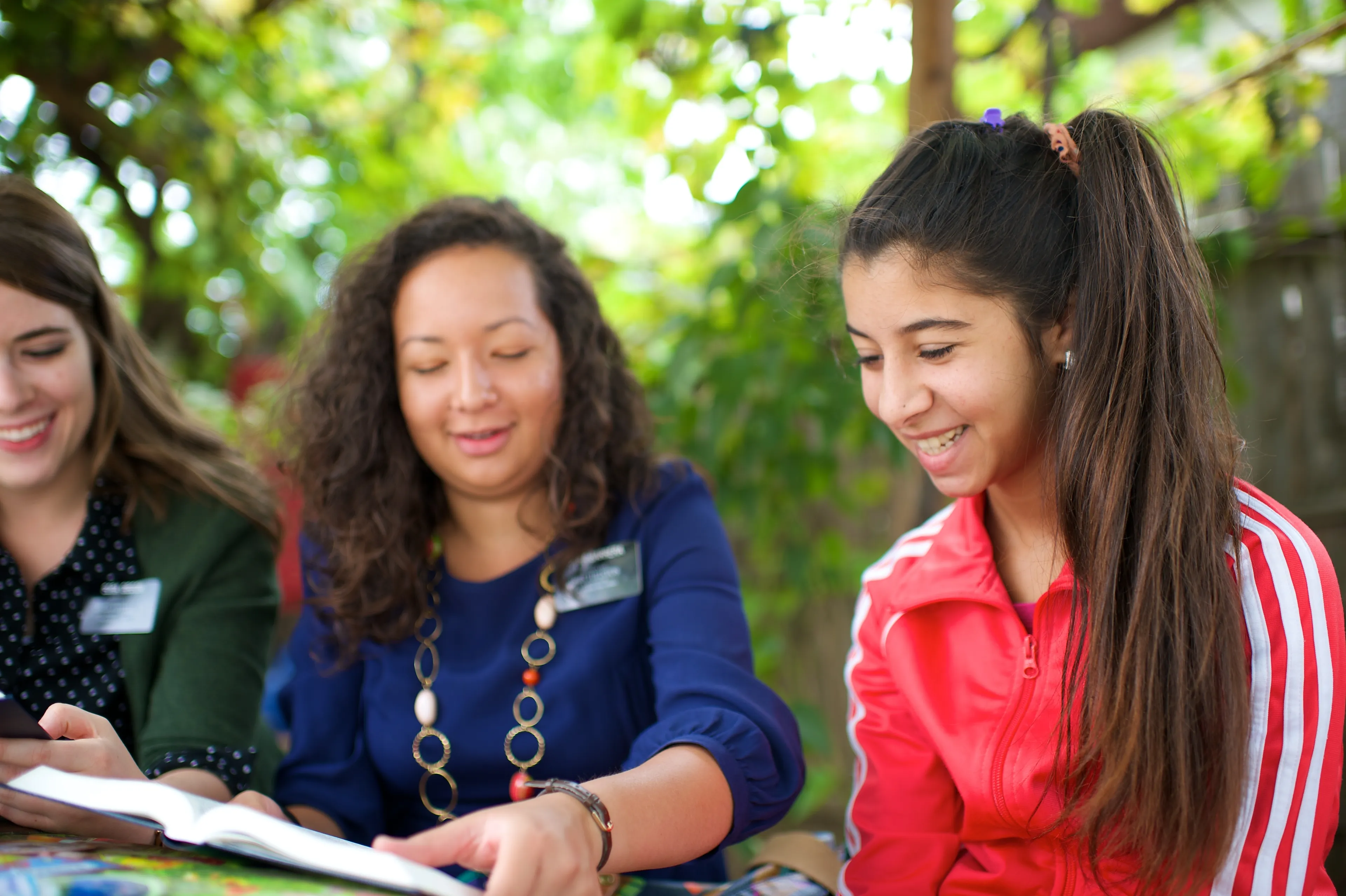 Two sister missionaries sit outside, teaching a young woman.