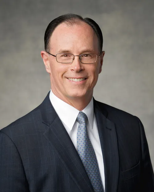 A portrait of W. Christopher Waddell wearing a black suit and a silver tie.
