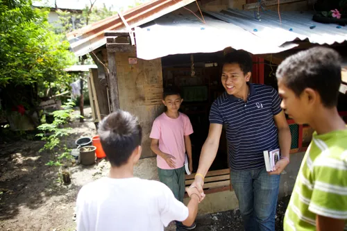A ministering brother carrying scriptures and shaking hands with a young man outside a home, with two other young men standing nearby.