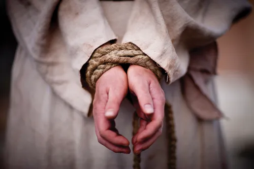 The hands of Christ tied together with a brown braided rope.