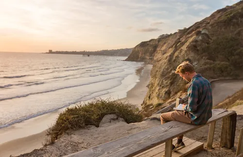 young adult reading scriptures by the beach