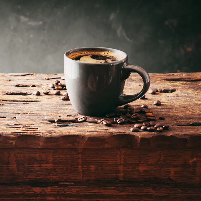 A steaming coffee mug on a table with coffee beans one of the don'ts of the word of wisdom