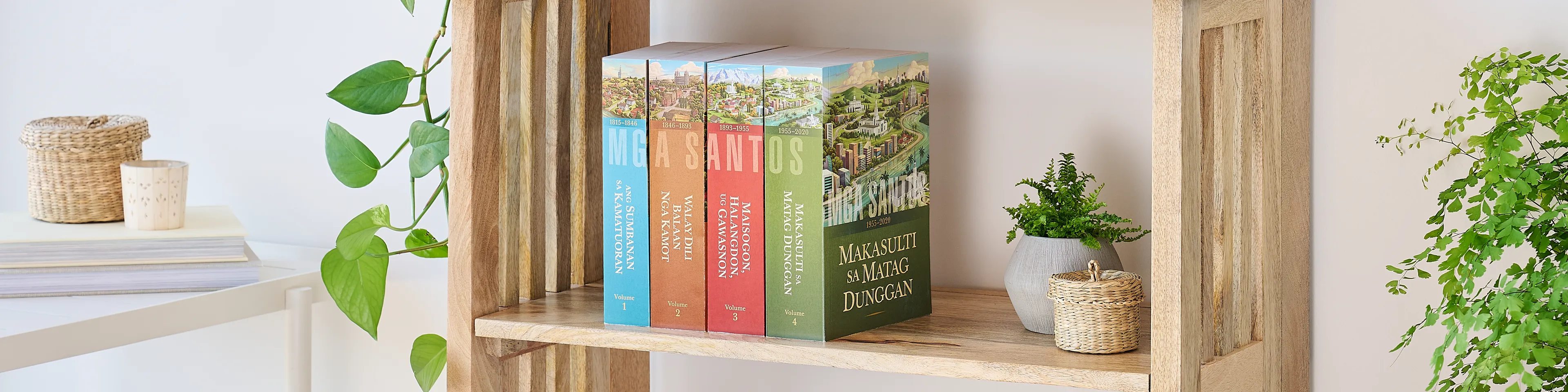 Picture of the book series, 'Saints' volume 1-4 (Cebuano edition). Four volumes are arranged on the middle shelf of a wooden bookshelf along with plants.