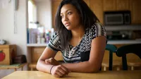 A thoughtful young woman sitting at a kitchen table.