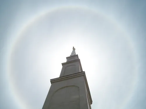 The main spire on the Lima Peru Temple seen from below, with the angel Moroni and the bright sky beyond.