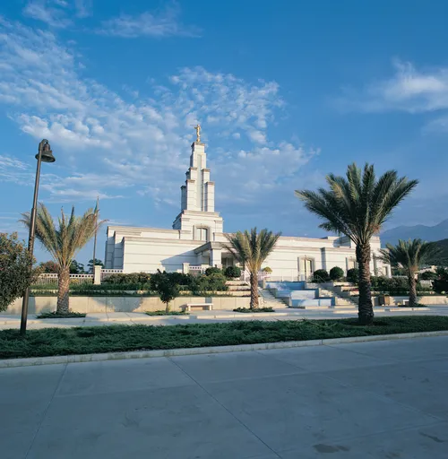 A view from afar of the Monterrey Mexico Temple, with its landscape of palm trees and other plants framing the entrance.