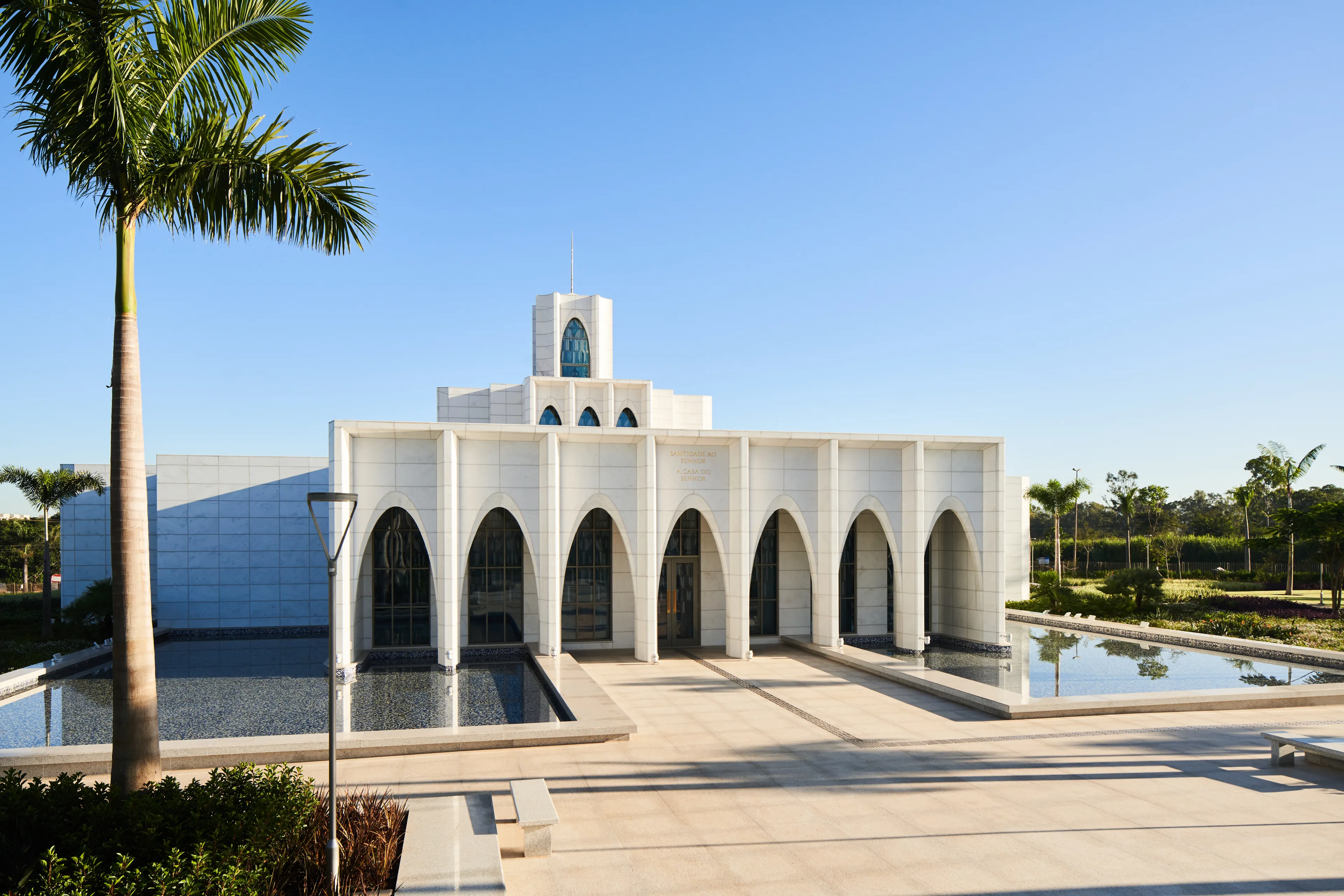 Exterior of the Brasilia Brazil Temple. It features the front of the temple, the entrance area, and trees nearby. Image was taken during the day.